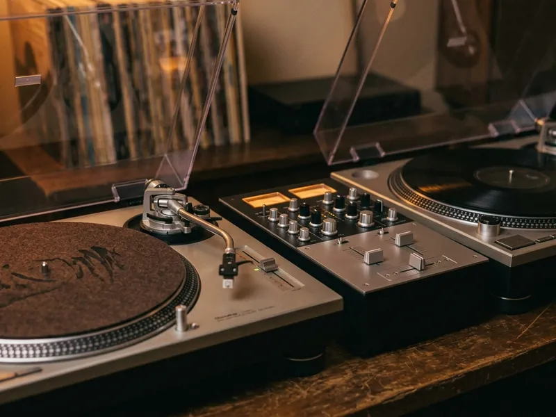Two silver direct-drive DJ turntables with a mixer between them